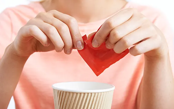 a woman adding artificial sweetener to a cup