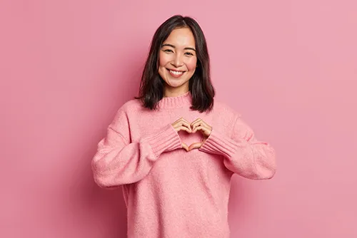 girl in pink sweater making a heart with her hands