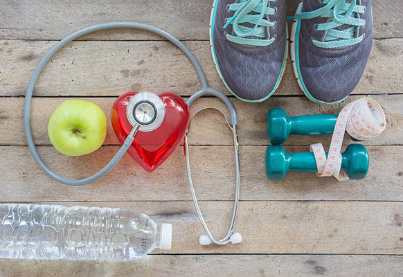 shoes, dumbells, water bottle, apple and a stethoscope on top of a plastic heart