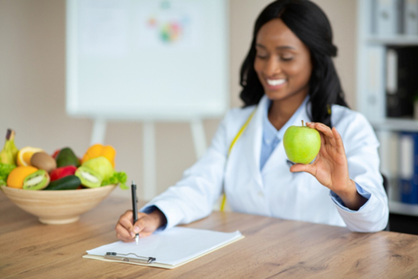 female doctor writes notes while holding an apple